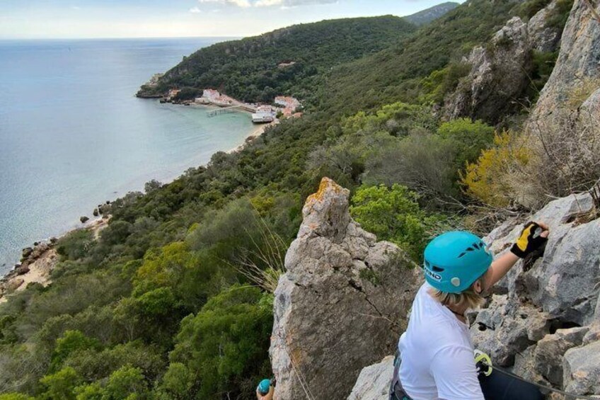 Una persona escalando un risco con vistas a una zona costera, una playa y vegetación. 4