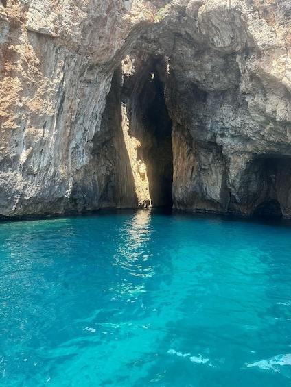 A natural rock formation with a cave entrance and clear blue water. 2