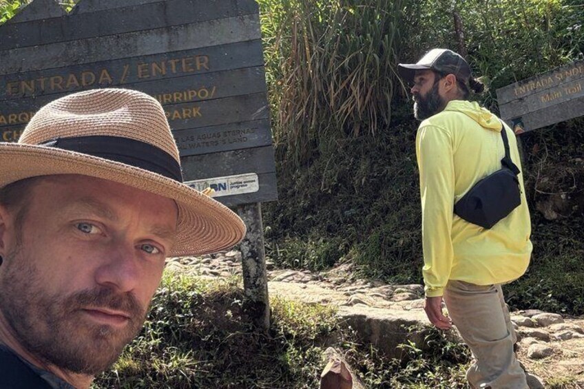 A person wearing a straw hat and a yellow shirt walking near a sign that reads 'ENTRADA / ENTER' and 'MAM Trail.' 1