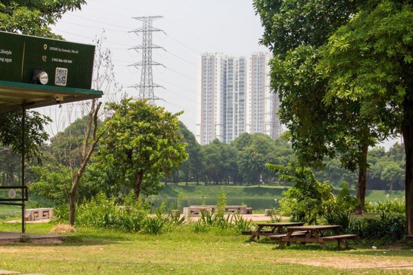 A park with picnic tables, a green shelter, and a tall building in the background. 3