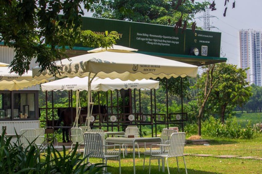 A park with a covered seating area, a signboard, and a building in the background. 5