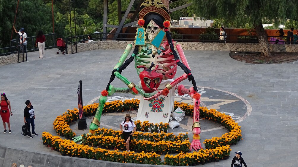 Una gran escultura de esqueleto rodeada por un círculo de flores de cempasúchil. 3