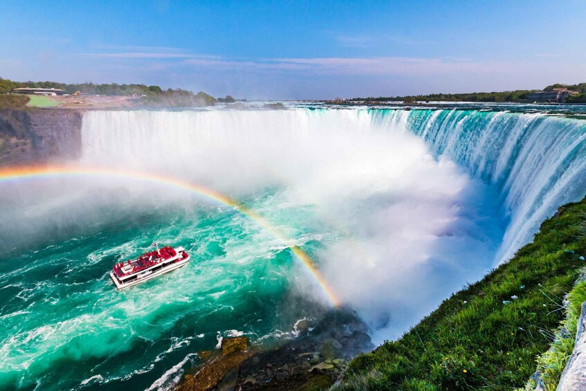 A large waterfall with a rainbow, a boat in the water, and a forested area in the background. 1