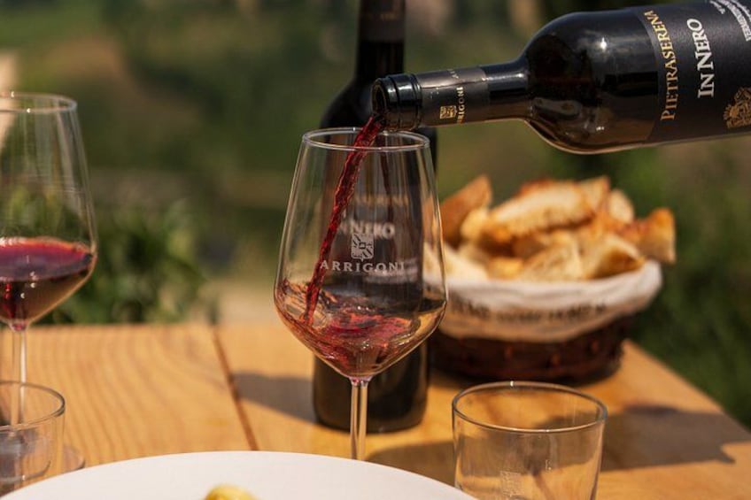 A bottle of wine being poured into a glass, a basket of bread, and a plate with a lemon on a wooden table. 4