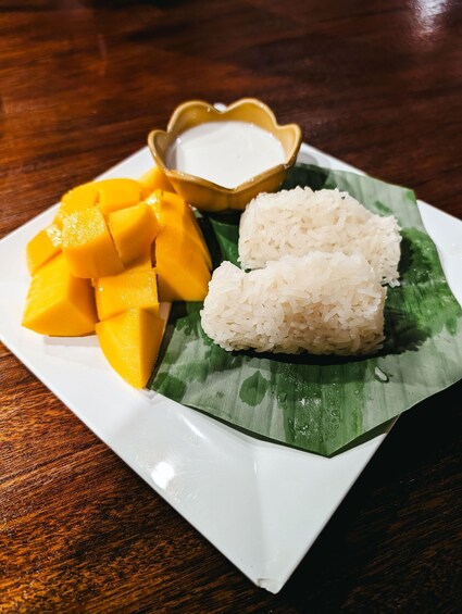 A plate of white rice and mango chunks on a banana leaf, with a small bowl of white sauce. 2