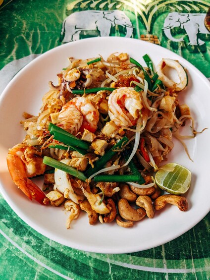A plate of Pad Thai with shrimp, noodles, green onions, and lime. 1