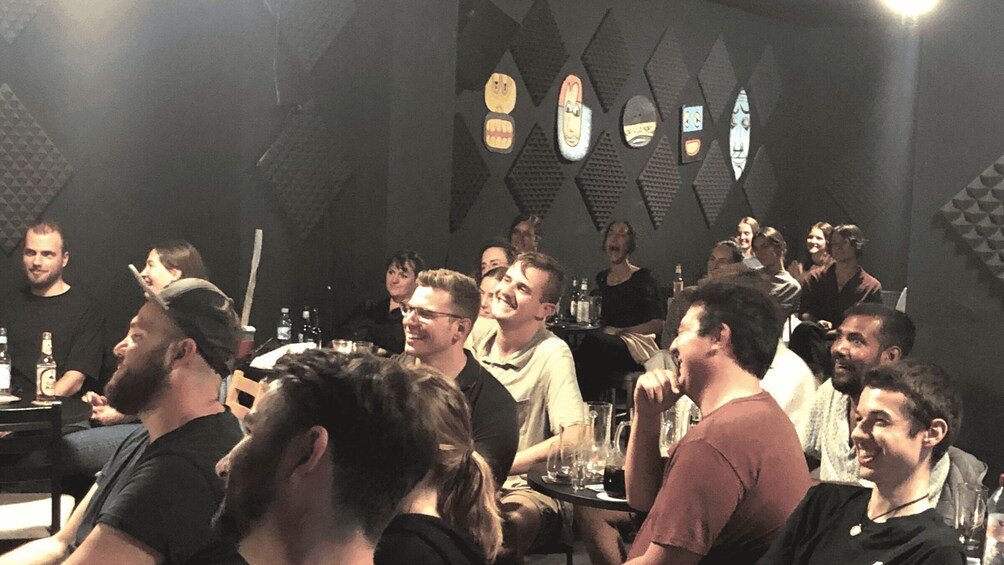 A group of people seated at tables in a dimly lit room with geometric wall patterns. 3