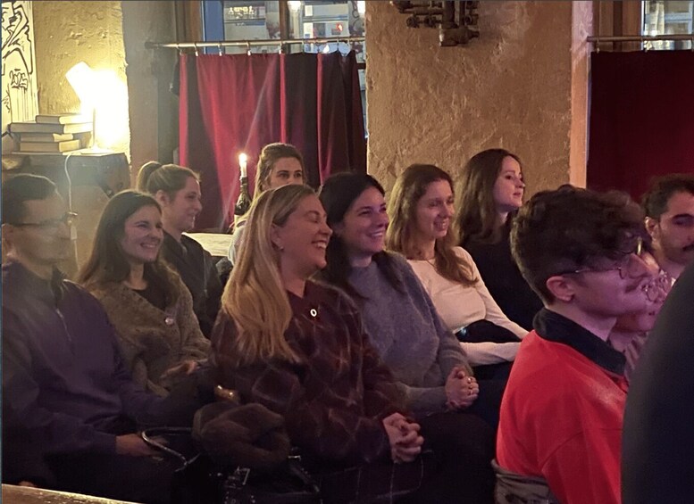 A group of people seated in an indoor setting with a stage or performance area in the background. 2