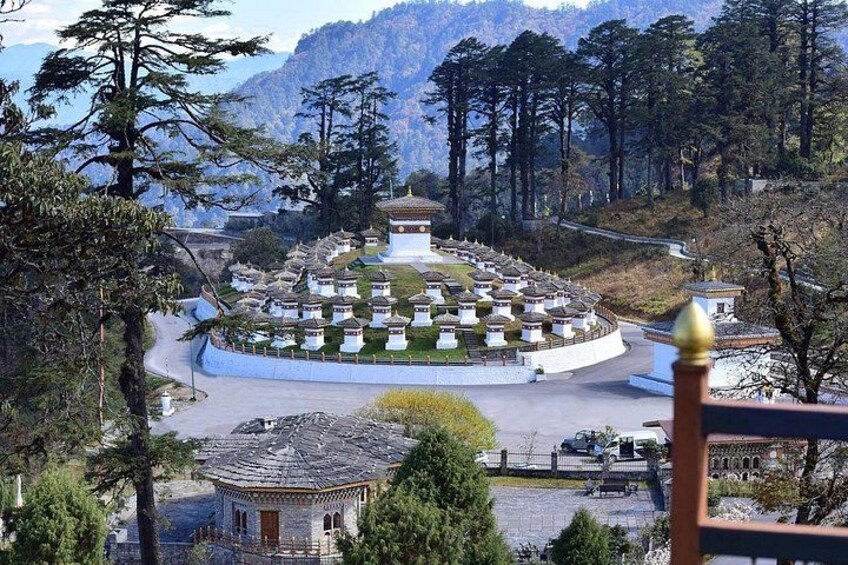 A circular arrangement of buildings with a central structure, surrounded by trees and a mountainous backdrop. 3