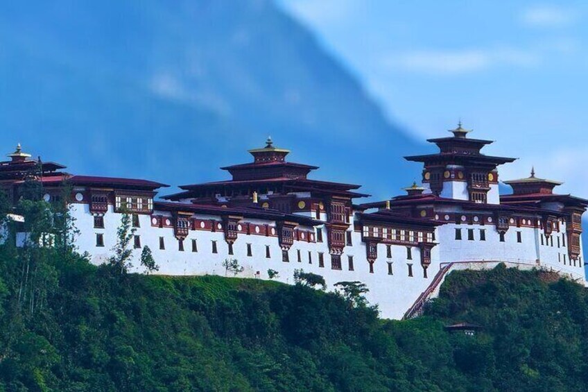 A traditional multi-tiered building with a white facade and red accents, surrounded by lush greenery. 1