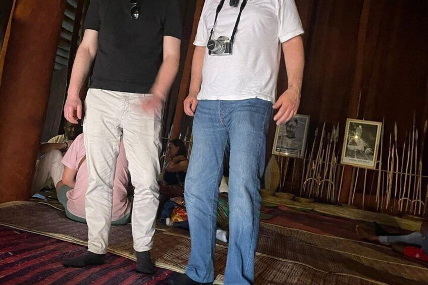Two people standing indoors, one wearing a black shirt and beige pants, the other in a white shirt and blue jeans. 2