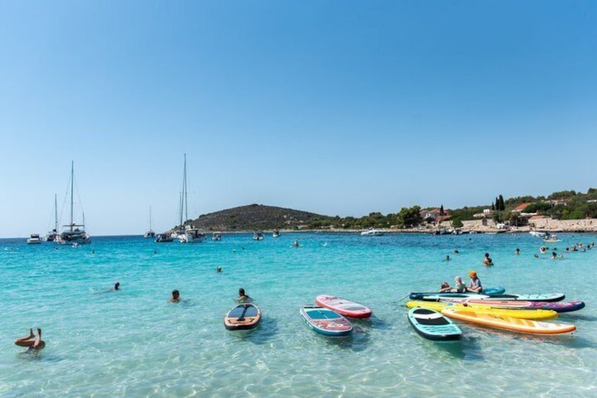 A beach with clear turquoise water, people swimming, and several colorful kayaks and paddleboards. 3
