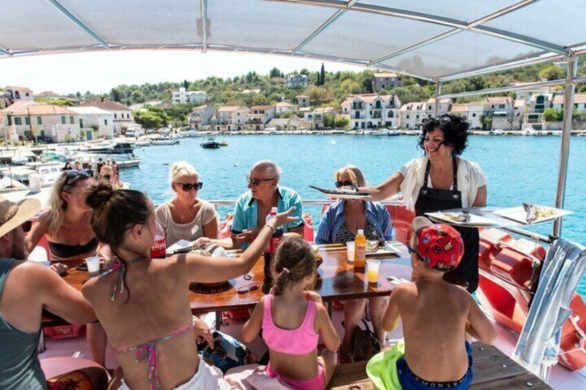 A group of people dining on a boat with a marina and buildings in the background. 4