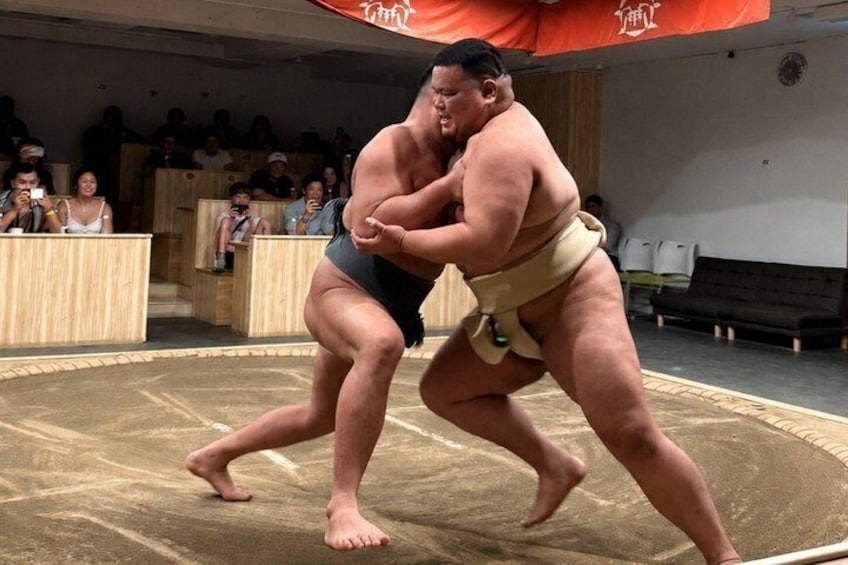 Two sumo wrestlers in a ring, with an audience in the background. 1