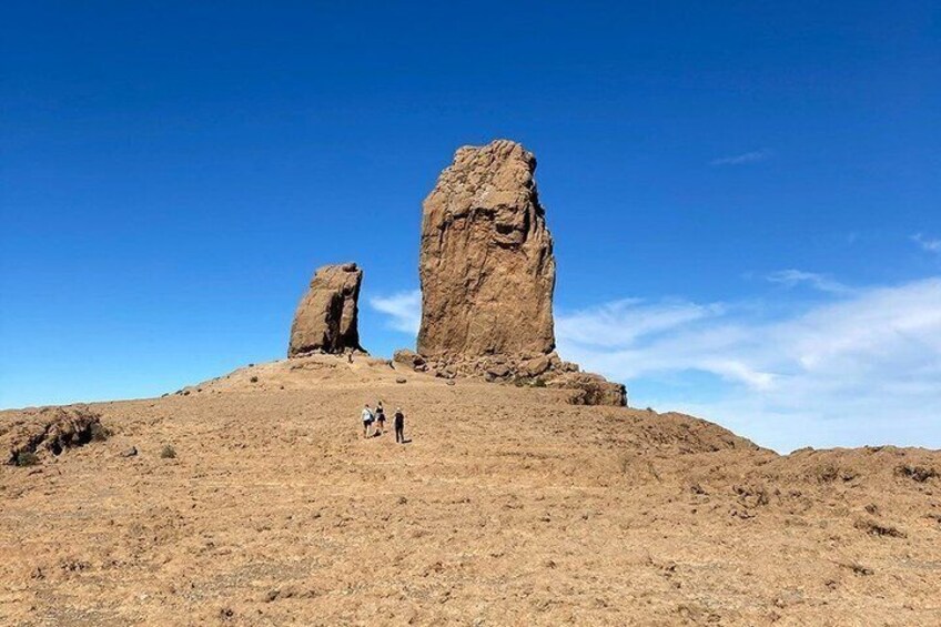 A desert landscape with two prominent rock formations and a few hikers. 4