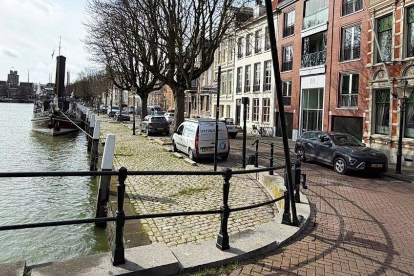 A canal with a row of parked cars and a building with a red facade. 2