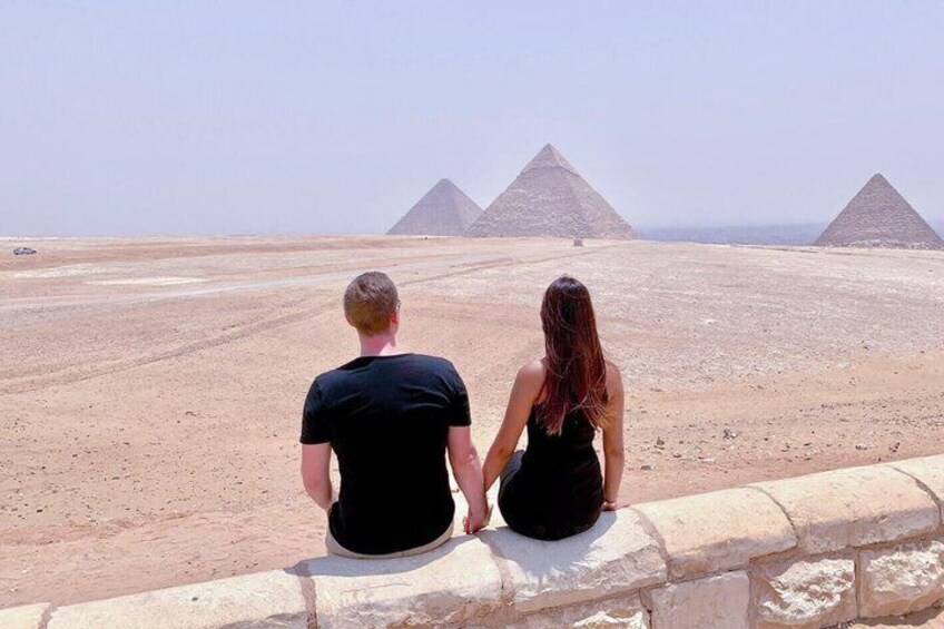 Two people sitting on a stone wall overlooking the pyramids. 1