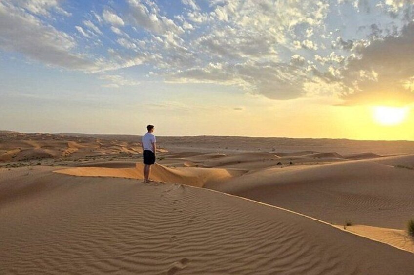 A person standing on a sand dune with a desert landscape and a sunset in the background. 5