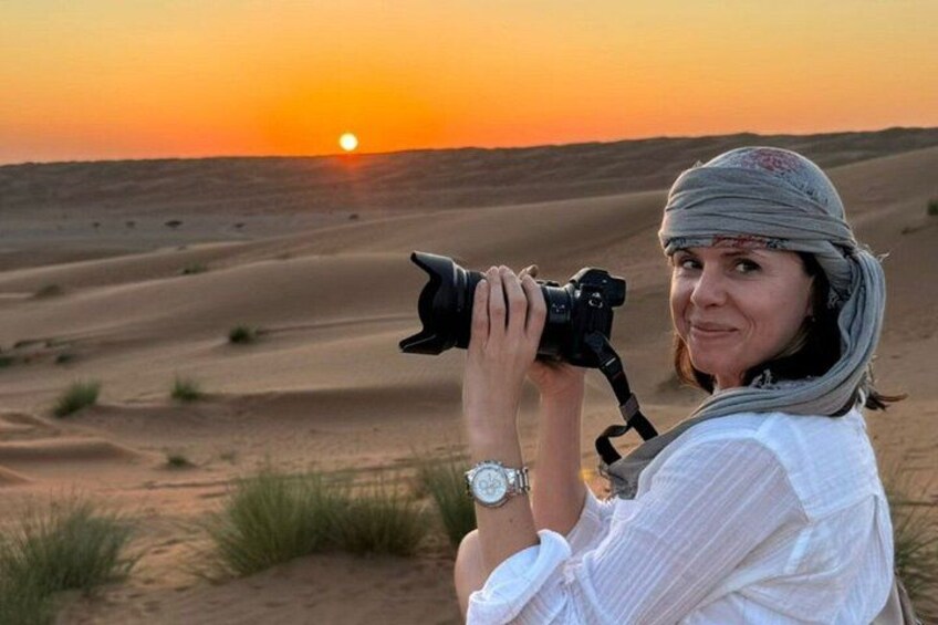 A person taking a photo with a camera in a desert landscape during sunset. 4