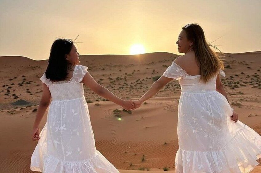Two people holding hands in a desert landscape at sunset. 1