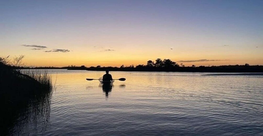 A person kayaking on a calm body of water during sunset. 3