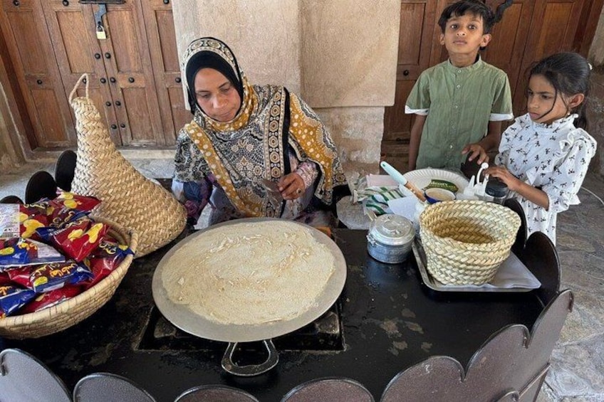 Una mujer y dos niños preparando comida en una mesa con un pan plano grande, tazones y cestas. 4