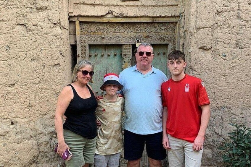 Una familia de cuatro personas de pie frente a una pared con textura y una puerta. 2