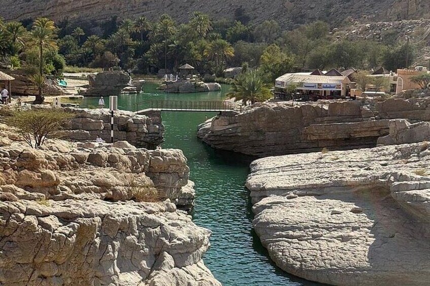 A river flowing through a rocky landscape with buildings and palm trees in the background. 2