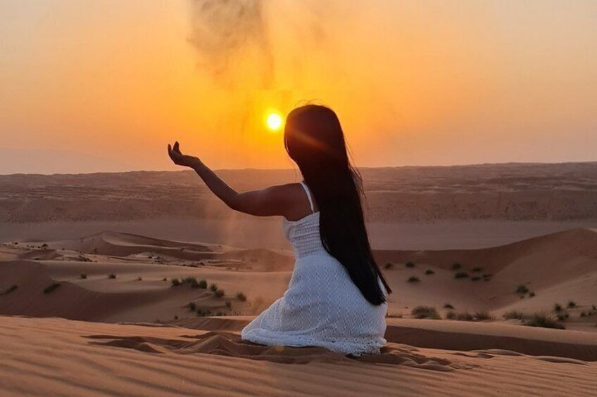 A person in a white dress kneeling on sand dunes at sunset. 3