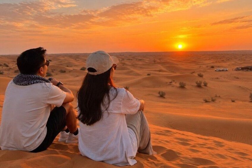 Two people sitting on sand dunes during sunset. 1