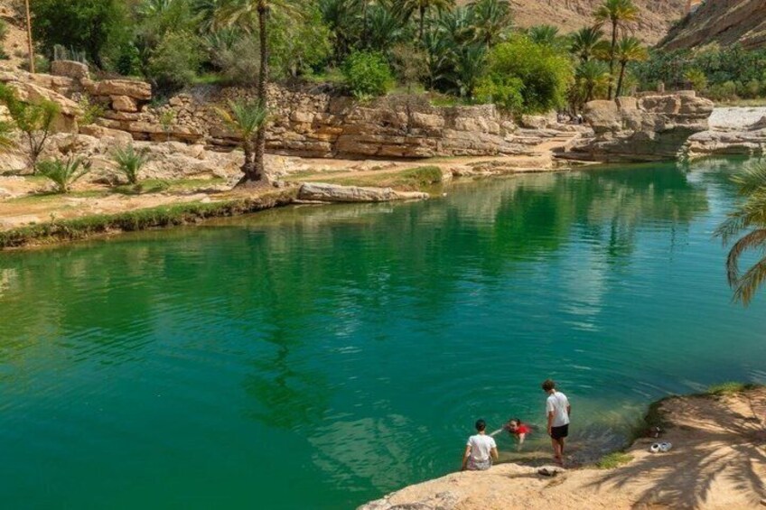 A clear turquoise river with rocky banks, palm trees, and a few people standing by the edge. 5