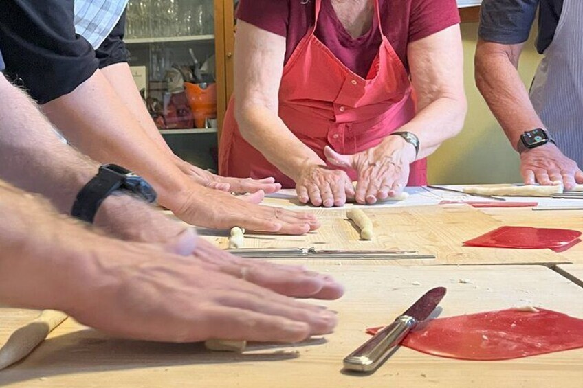 People rolling dough on a wooden surface with a rolling pin and a knife. 3