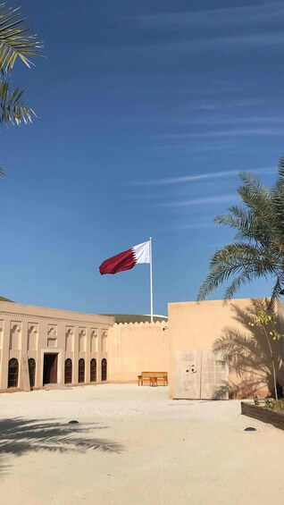 A flagpole with a flag, a building with arched windows, and palm trees. 2