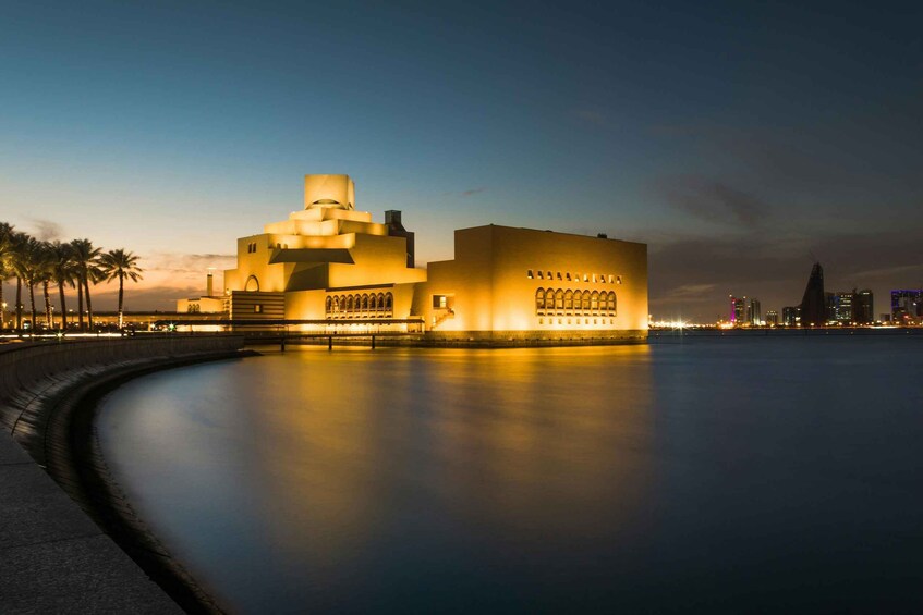 A modern architectural building with a unique design, situated by a waterfront with palm trees and a city skyline in the background. 4