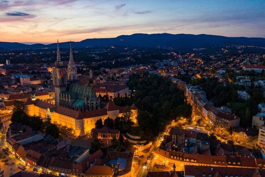 A cityscape at dusk with illuminated buildings and a prominent church with a tall spire. 1