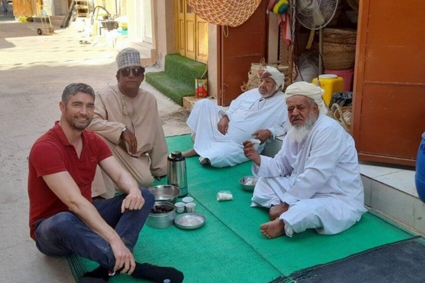 Quatre personnes sont assises sur un tapis devant un bâtiment dont le sol est vert. 4