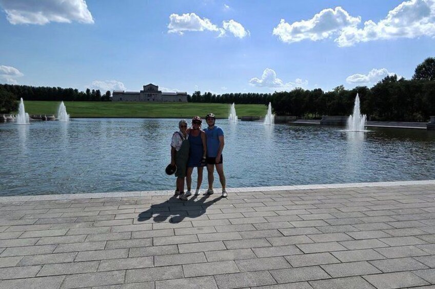 A group of people standing by a fountain with a large building in the background. 2