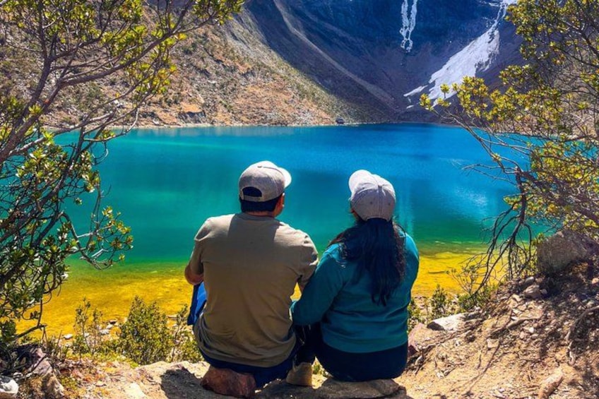 Two people sitting by a lake with mountains in the background. 3