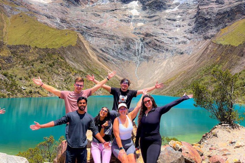 A group of people standing on a rocky outcrop with a lake and mountains in the background. 2