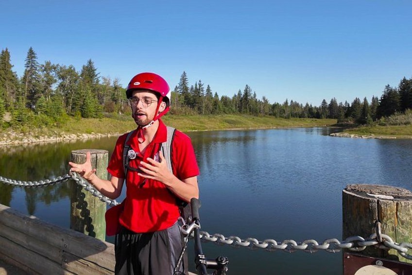 A person in a red shirt and helmet standing on a dock by a calm lake with trees in the background. 4