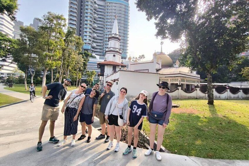 A group of people posing in a park with a monument and modern buildings in the background. 4