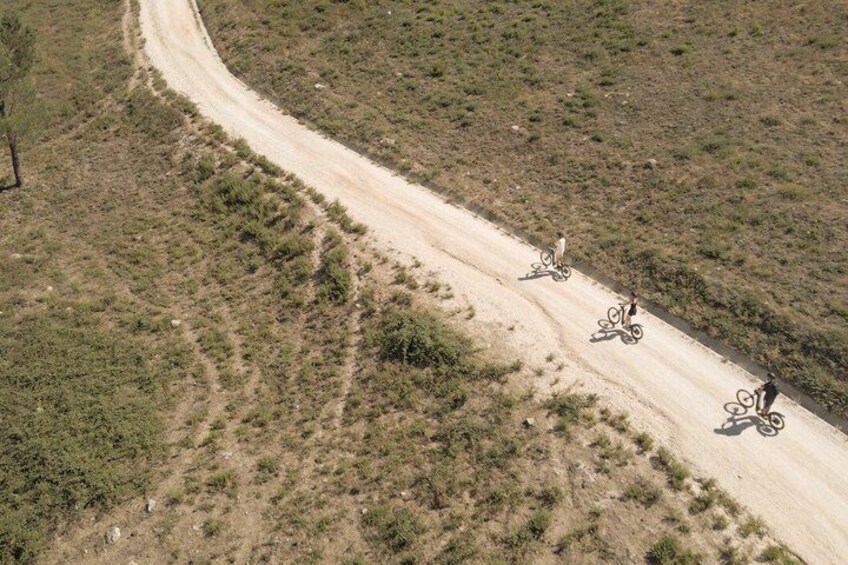 A dirt road curving through a dry, grassy landscape with three cyclists riding along it. 4