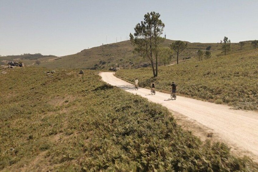 A dirt road winding through a hilly landscape with sparse vegetation and a few people riding bicycles. 3