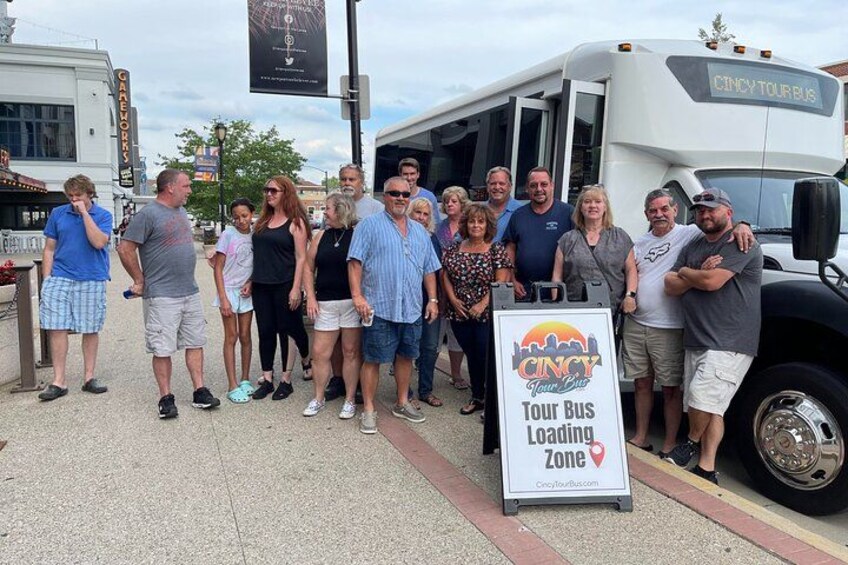 Un grupo de personas de pie frente a un autobús turístico con un letrero que dice 'Cincinnati Tour Bus Loading Zone'. 2