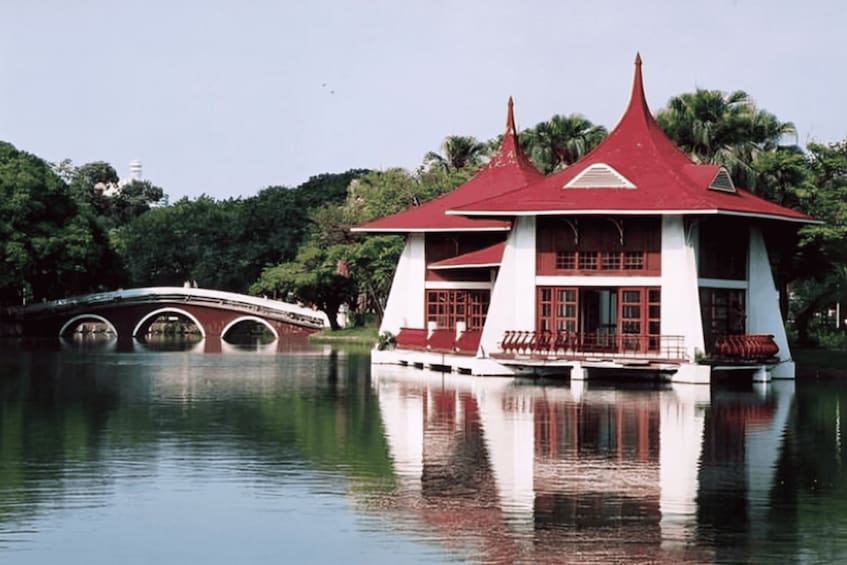A traditional building with a red roof and white walls, situated on a lake with a bridge in the background. 2