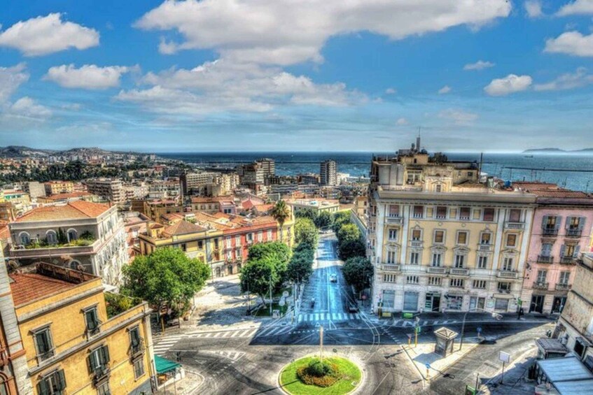A coastal cityscape with a prominent street leading to a waterfront, surrounded by historic buildings and a clear sky. 5