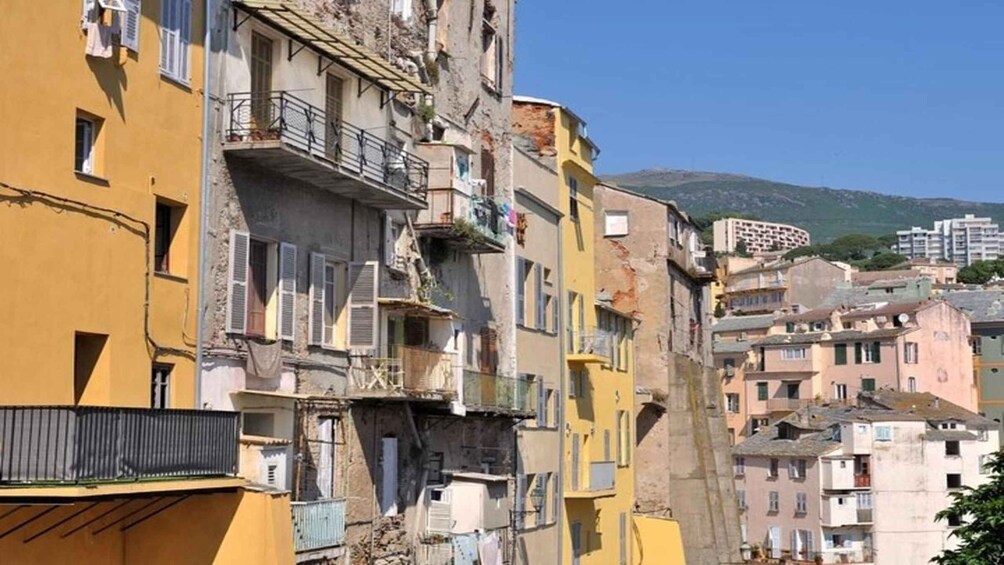 A row of colorful buildings with balconies, some with laundry hanging out to dry, and a mountain in the background. 1