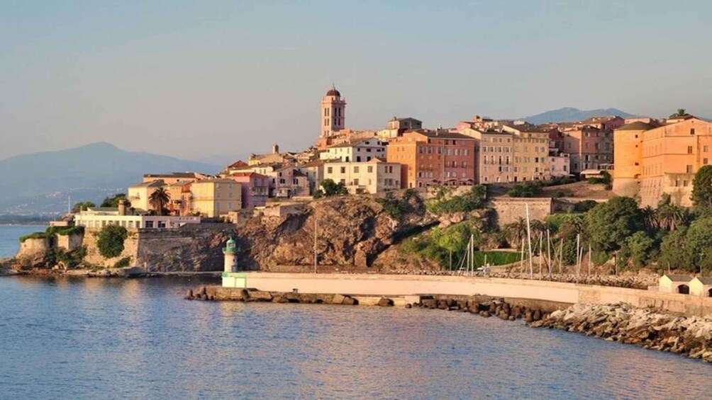 A coastal town with buildings, a lighthouse, and mountains in the background. 2