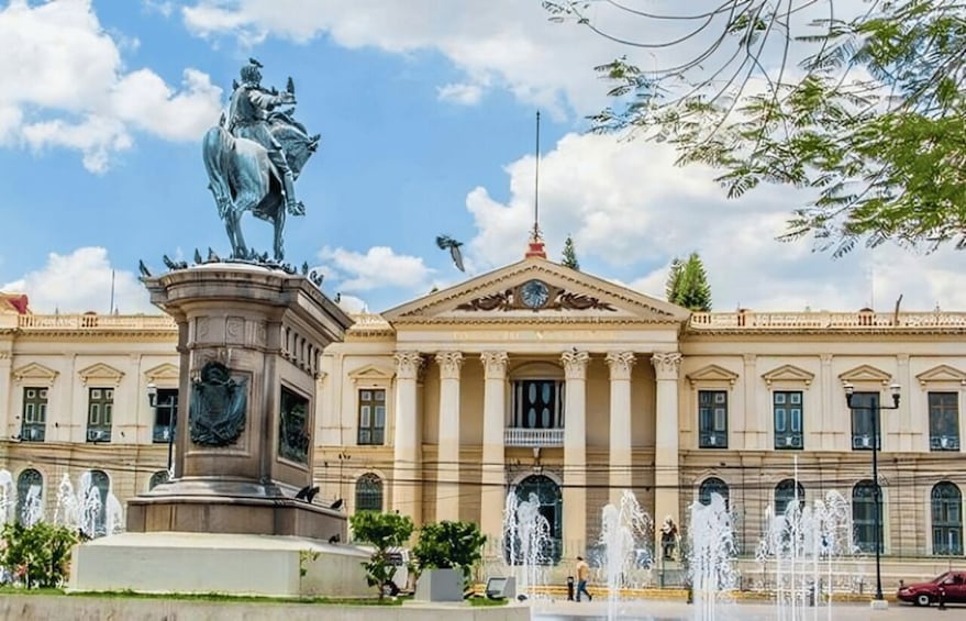 A classical building with a central statue, fountains, and a clear sky. 3