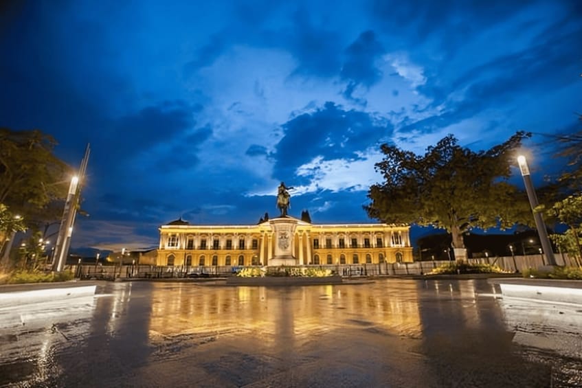 A historic building with a statue in front, surrounded by trees and a wet reflective ground. 2